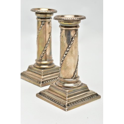 128 - A PAIR OF CANDLE STICKS, Corinthian candlesticks, on square stepped bases (one with a weighted base ... 