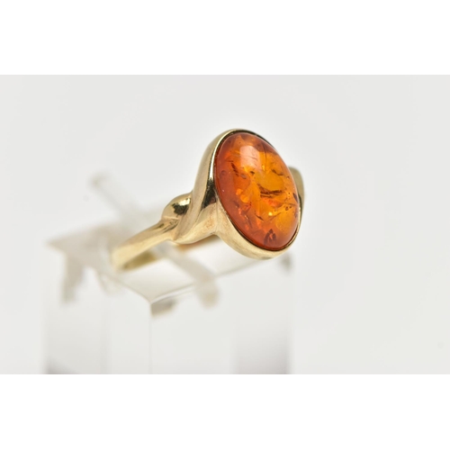 47 - A 9CT YELLOW GOLD AMBER CABOCHON RNIG, collet set with an oval cut amber cabochon, twist detail to t... 