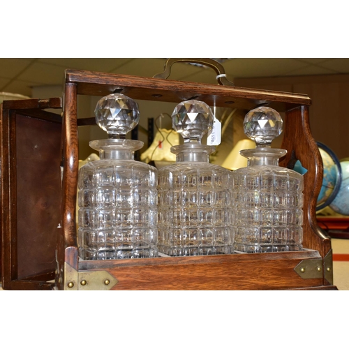 471 - AN EDWARDIAN TANTULUS, with brass mounts, containing three square cut crystal decanters each with a ... 