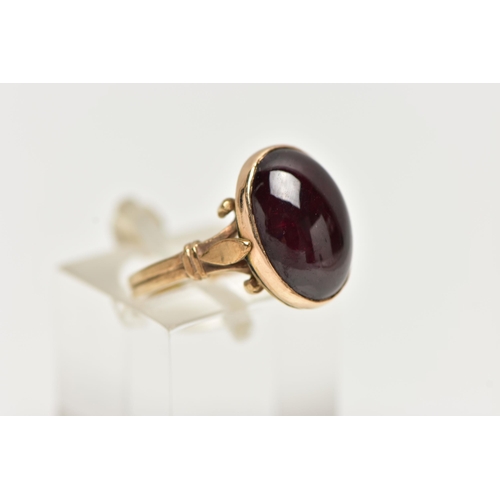 82 - A 9CT YELLOW GOLD GARNET SINGLE STONE RING, the oval garnet cabochon, within a collet setting, to th... 