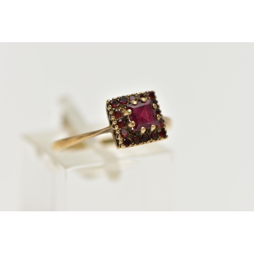 12 - A 9CT GOLD GEMSET RING, a square cut garnet, set with a surround of sixteen circular cut garnets, le... 