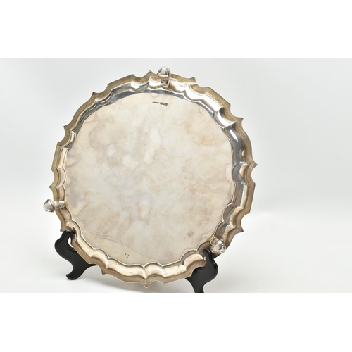 67 - A GEORGE V SILVER SALVER OF CIRCULAR FORM WITH PIE CRUST RIM, engraved narrow border, on three scrol... 