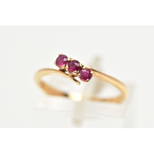 15 - A THREE STONE RUBY RING, three circular cut rubies prong set in yellow metal, leading on to a bypass... 