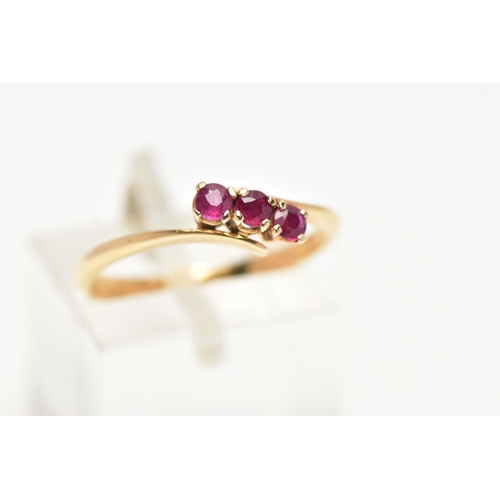 15 - A THREE STONE RUBY RING, three circular cut rubies prong set in yellow metal, leading on to a bypass... 