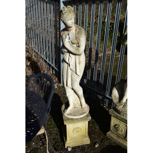 906 - A WEATHERED COMPOSITE GARDEN FIGURE, of a scantily clad lady in flowing robes, on a separate plinth,... 