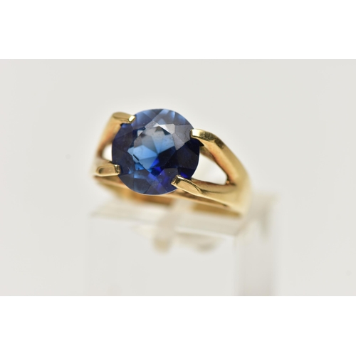 12 - A YELLOW METAL GEM SET RING, a circular cut synthetic blue sapphire, in a four prong setting, bifurc... 