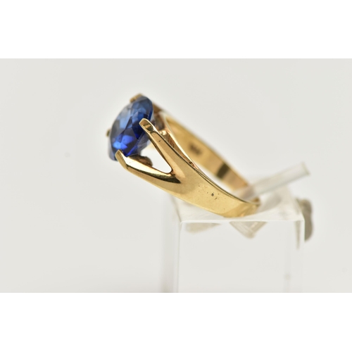 12 - A YELLOW METAL GEM SET RING, a circular cut synthetic blue sapphire, in a four prong setting, bifurc... 