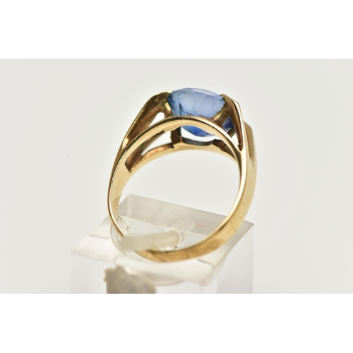 12 - A YELLOW METAL GEM SET RING, a circular cut synthetic blue sapphire, in a four prong setting, bifurc... 