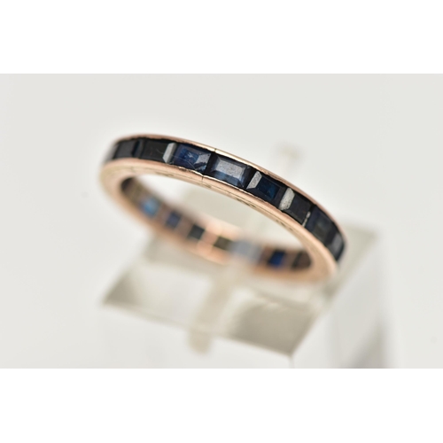 52 - A ROSE METAL FULL ETERNITY RING, set with a full row of square cut deep blue sapphires, channel set ... 