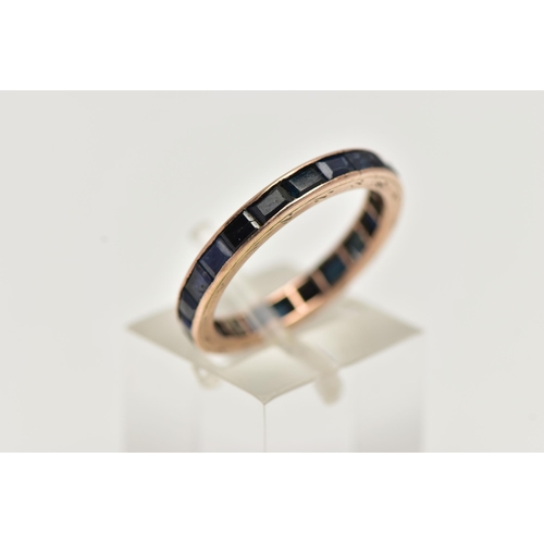 52 - A ROSE METAL FULL ETERNITY RING, set with a full row of square cut deep blue sapphires, channel set ... 