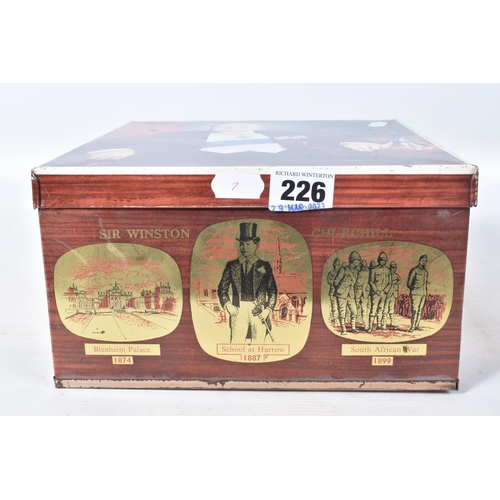 226 - A WINSTON CHURCHILL BISCUIT TIN, containing a hallmarked silver cigarette holder, a cased set of bin... 