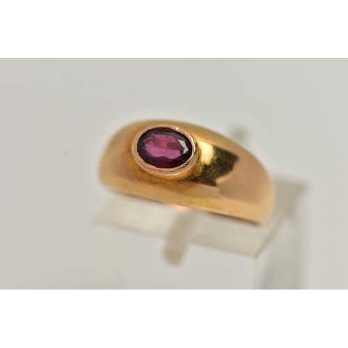 23 - A YELLOW METAL GARNET SET RING, set with an oval cut garnet in a raised collet setting, to a taperin... 