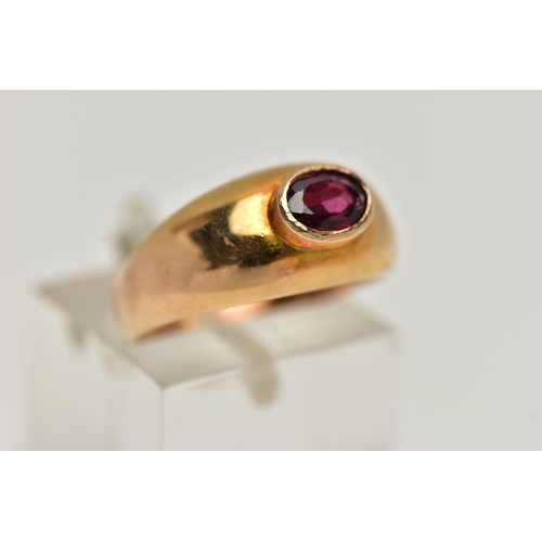 23 - A YELLOW METAL GARNET SET RING, set with an oval cut garnet in a raised collet setting, to a taperin... 