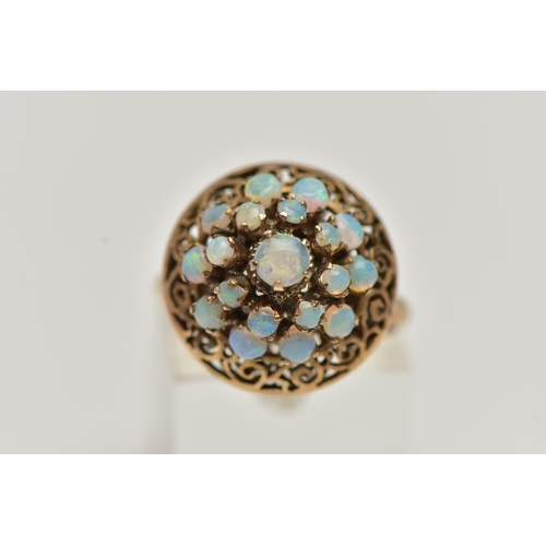 25 - A YELLOW METAL OPAL RING, tiered ring set with nineteen opal cabochons, to the openwork scroll surro... 