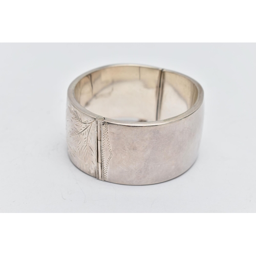 58 - A SILVER HINGED BANGLE, a wide bangle engraved with a floral and foliage design, approximate width 3... 