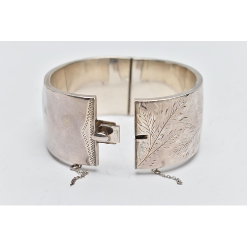 58 - A SILVER HINGED BANGLE, a wide bangle engraved with a floral and foliage design, approximate width 3... 