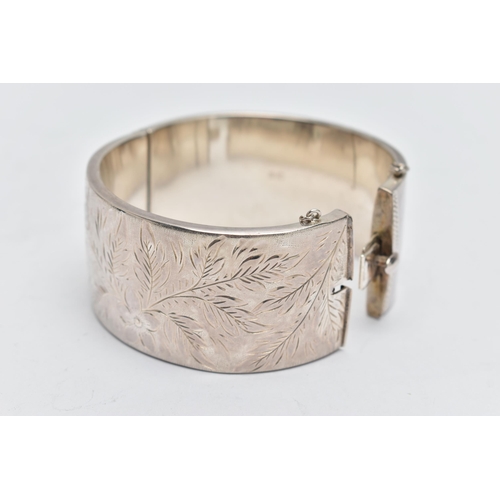 58 - A SILVER HINGED BANGLE, a wide bangle engraved with a floral and foliage design, approximate width 3... 