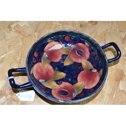 451 - A WILLIAM MOORCROFT TWIN HANDLED FOOTED BOWL DECORATED WITH POMEGRANATE PATTERN ON A DARK BLUE MOTTL... 