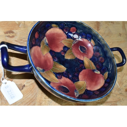 451 - A WILLIAM MOORCROFT TWIN HANDLED FOOTED BOWL DECORATED WITH POMEGRANATE PATTERN ON A DARK BLUE MOTTL... 