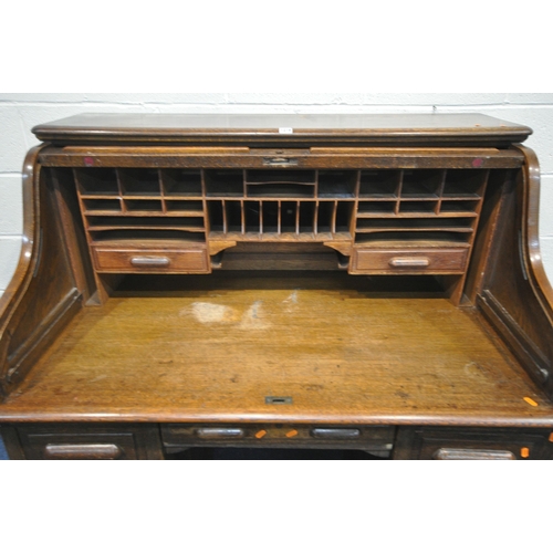 1216 - AN EARLY 20TH CENTURY OAK ROLL TOP DESK, enclosing an arrangement of shelving and two drawers, over ... 