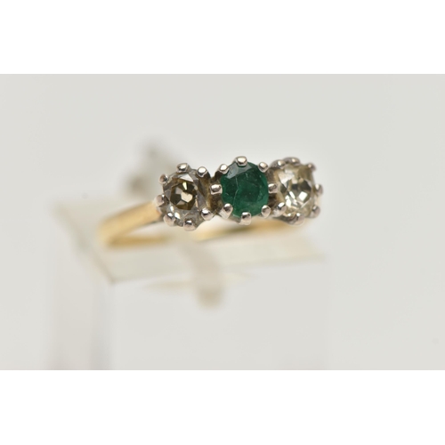 38 - A YELLOW  METAL EMERALD AND DIAMOND THREE STONE RING, centring on an oval cut emerald, flanked with ... 