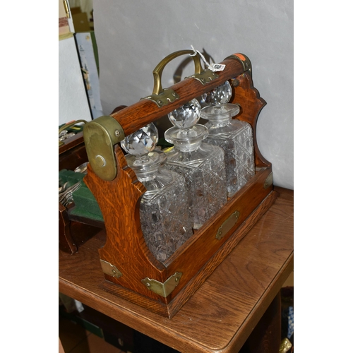 462 - AN EDWARDIAN OAK TANTULUS, with three decanters, original stoppers (one chipped at base), locking me... 