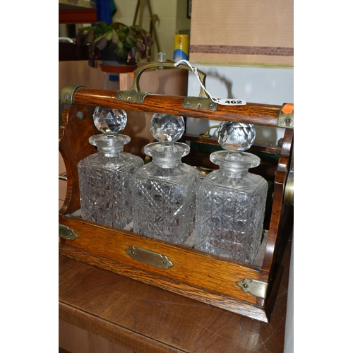 462 - AN EDWARDIAN OAK TANTULUS, with three decanters, original stoppers (one chipped at base), locking me... 