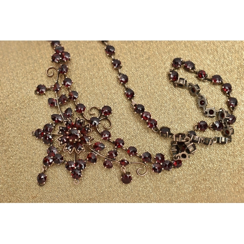 135 - A BOHEMIAN GARNET FESTOON STYLE NECKLACE, rose metal set with a cluster of circular cut garnets, lea... 