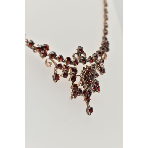 135 - A BOHEMIAN GARNET FESTOON STYLE NECKLACE, rose metal set with a cluster of circular cut garnets, lea... 