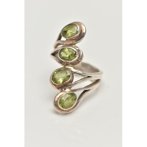 17 - A WHITE METAL PERIDOT DRESS RING, designed with a row of four oval cut peridots each collet set to a... 