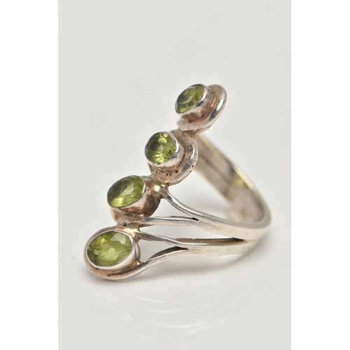 17 - A WHITE METAL PERIDOT DRESS RING, designed with a row of four oval cut peridots each collet set to a... 