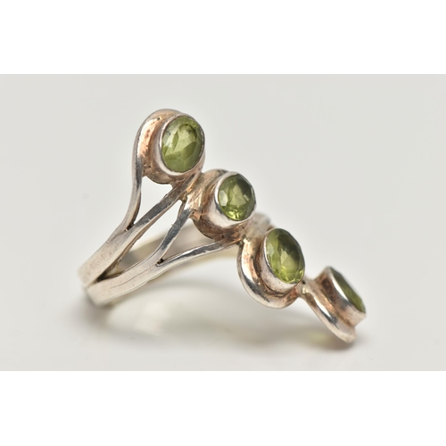 17 - A WHITE METAL PERIDOT DRESS RING, designed with a row of four oval cut peridots each collet set to a... 