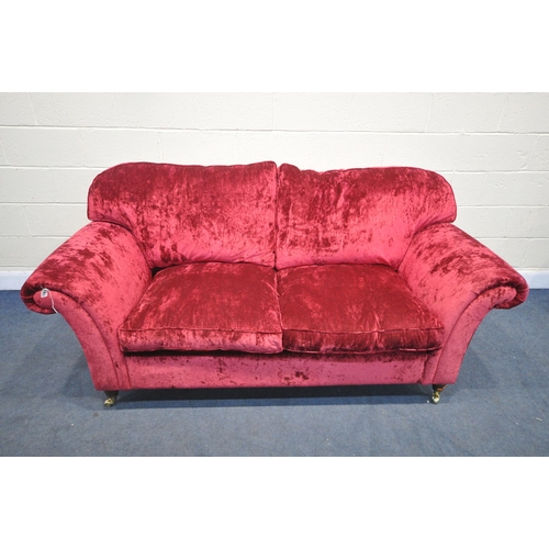 1304 - A RED VELVETEEN UPHOLSTERED TWO SEATER SETTEE, on turned legs and brass casters, length 202cm x dept... 