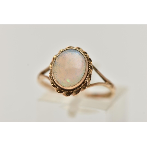 66 - A 9CT GOLD OPAL RING, oval cut opal cabochon, collet set with a fine rope twist surround, bifurcated... 