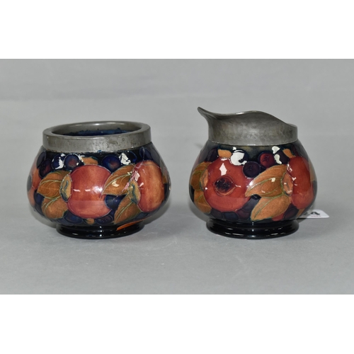 424 - A MOORCROFT POTTERY POMEGRANATE PATTERN CREAM JUG AND SUGAR BOWL, tube lined with fruit on a dark bl... 