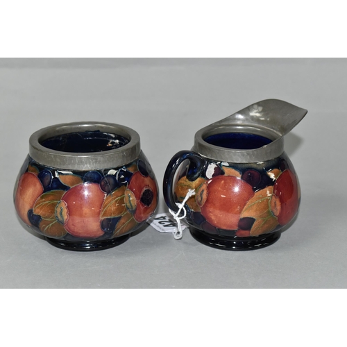 424 - A MOORCROFT POTTERY POMEGRANATE PATTERN CREAM JUG AND SUGAR BOWL, tube lined with fruit on a dark bl... 