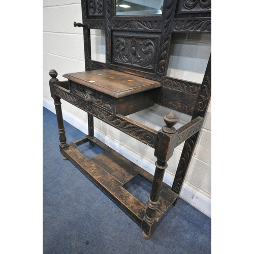 1215 - AN EARLY 20TH CENTURY CARVED OAK HALLSTAND, with ten hooks flanking a bevelled edge mirror, single d... 