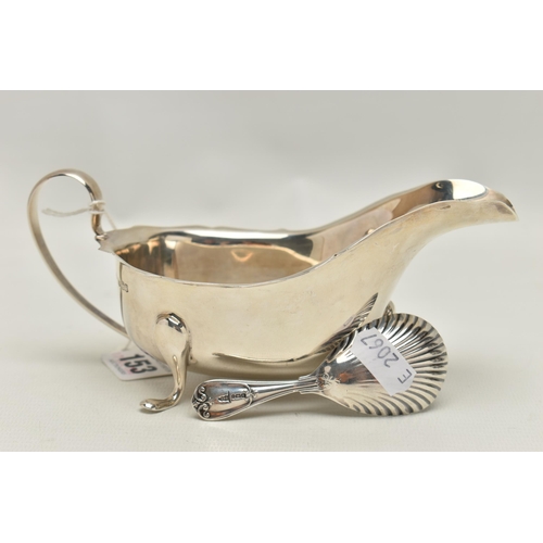 153 - A SILVER GRAVY BOAT AND A CADDY SPOON, polished form with wavy rim and scrolling handle, raised on t... 