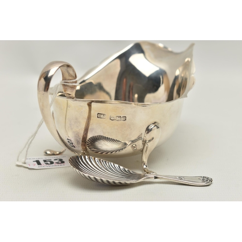 153 - A SILVER GRAVY BOAT AND A CADDY SPOON, polished form with wavy rim and scrolling handle, raised on t... 