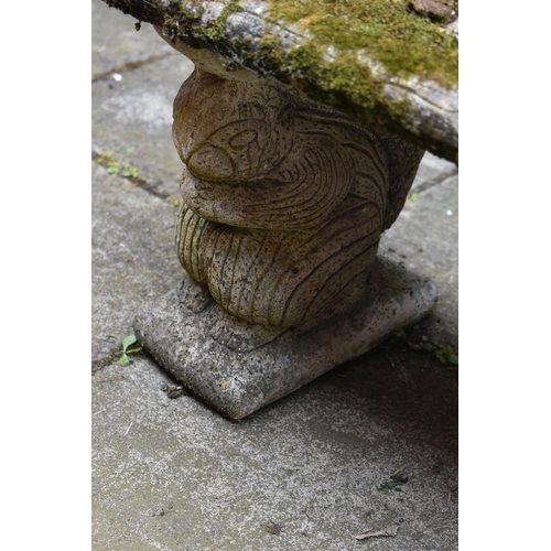 1023 - A WEATHERED COMPOSITE GARDEN BENCH, with a rectangular top, resting on twin pedestals depicting squi... 