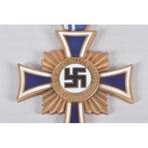 324 - A GERMAN GOLD MOTHERS CROSS, this comes on a length of ribbon and has the inscription on the back, C... 