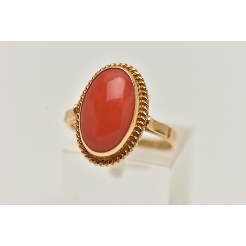 83 - A YELLOW METAL CORAL RING, oval coral cabochon, collet set in yellow metal with rope detail surround... 