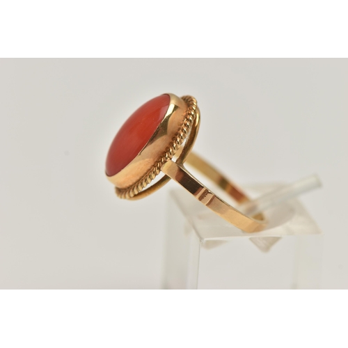 83 - A YELLOW METAL CORAL RING, oval coral cabochon, collet set in yellow metal with rope detail surround... 