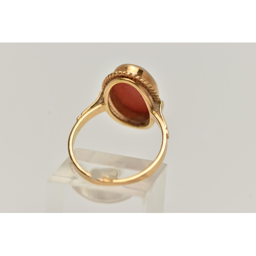 83 - A YELLOW METAL CORAL RING, oval coral cabochon, collet set in yellow metal with rope detail surround... 