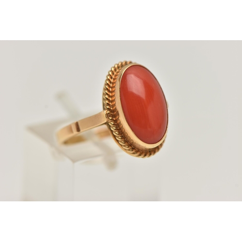 83 - A YELLOW METAL CORAL RING, oval coral cabochon, collet set in yellow metal with rope detail surround... 