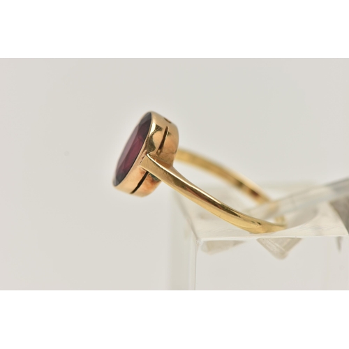 9 - A YELLOW METAL GARNET RING, set with an oval cut garnet, collet set to a polished band, stamped 18ct... 