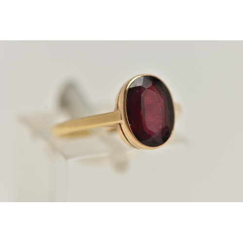 9 - A YELLOW METAL GARNET RING, set with an oval cut garnet, collet set to a polished band, stamped 18ct... 