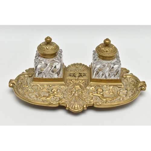 395A - A LATE VICTORIAN BRASS INKSTAND FITTED WITH TWO SQUARE MOULDED GLASS INKWELLS, the stand cast with s... 