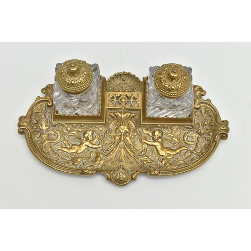 395A - A LATE VICTORIAN BRASS INKSTAND FITTED WITH TWO SQUARE MOULDED GLASS INKWELLS, the stand cast with s... 