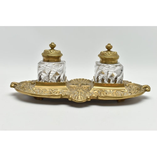 395A - A LATE VICTORIAN BRASS INKSTAND FITTED WITH TWO SQUARE MOULDED GLASS INKWELLS, the stand cast with s... 